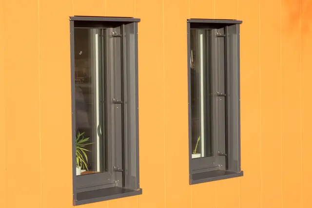 Anthrazitfarbene Fenster in orangefarbener Fassade