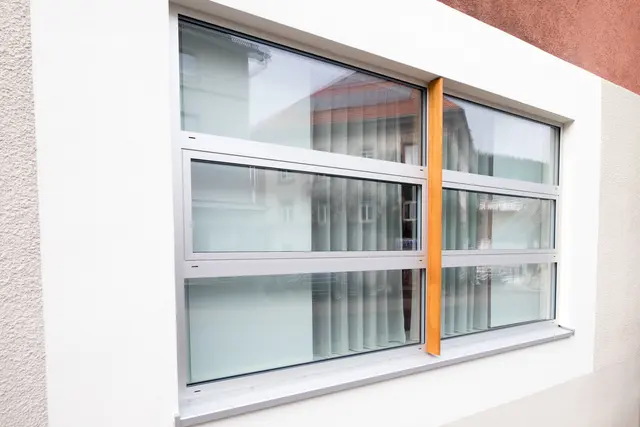 Fenster mit orangefarbenem Rahmen in heller Fassade
