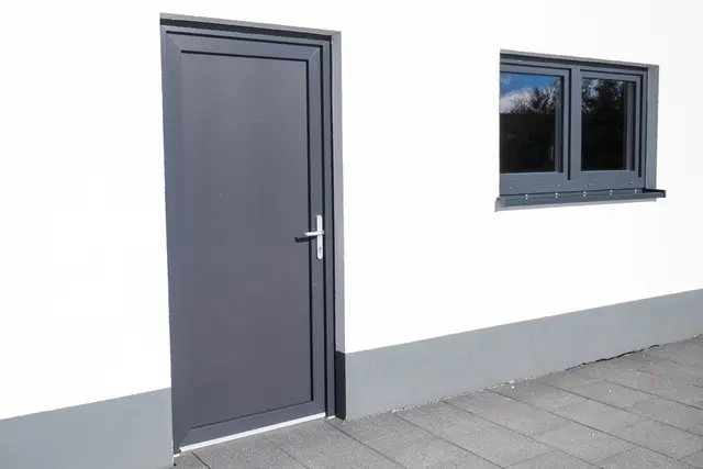 Graue Nebeneingangstür an einer hellen Fassade